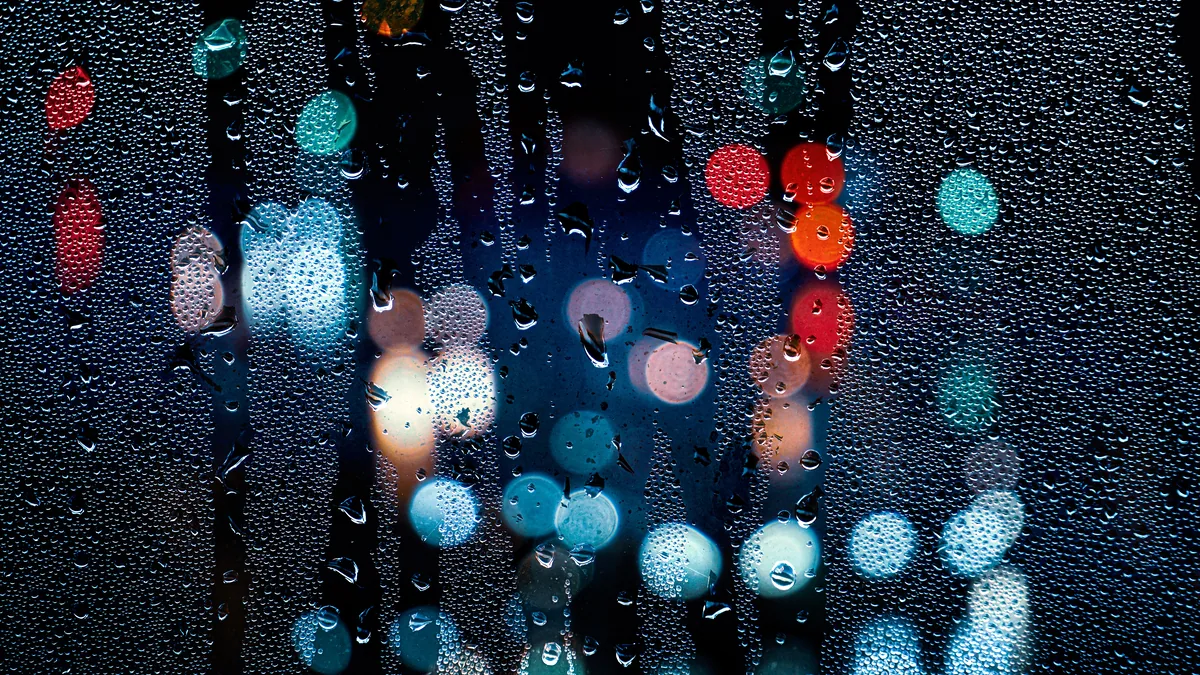Rain streaking a window while city lights blur gold outside.