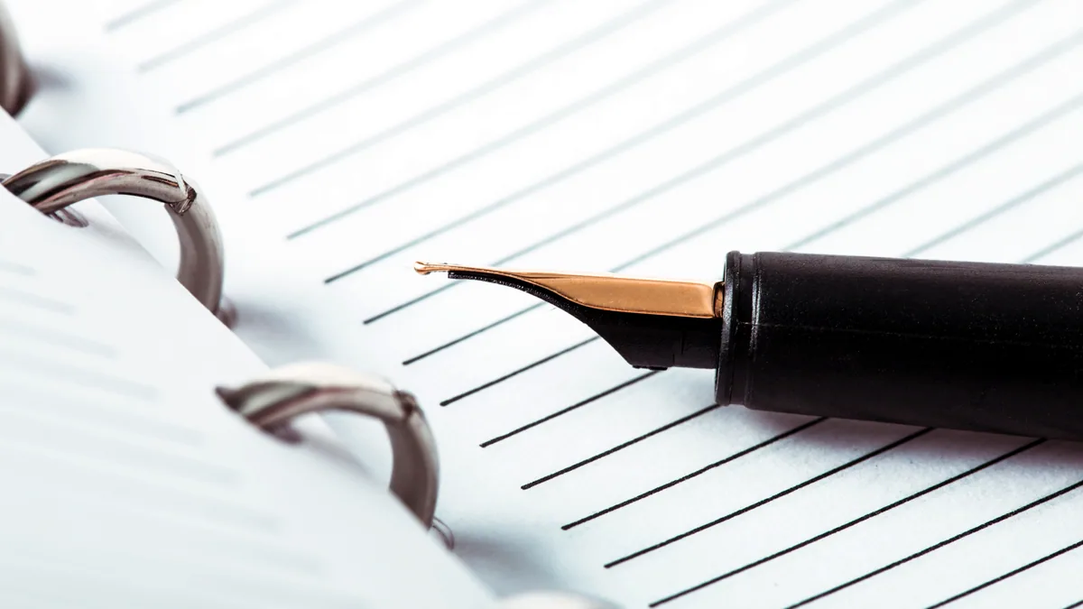 An ink pen resting on a sheet of ruled letter paper.