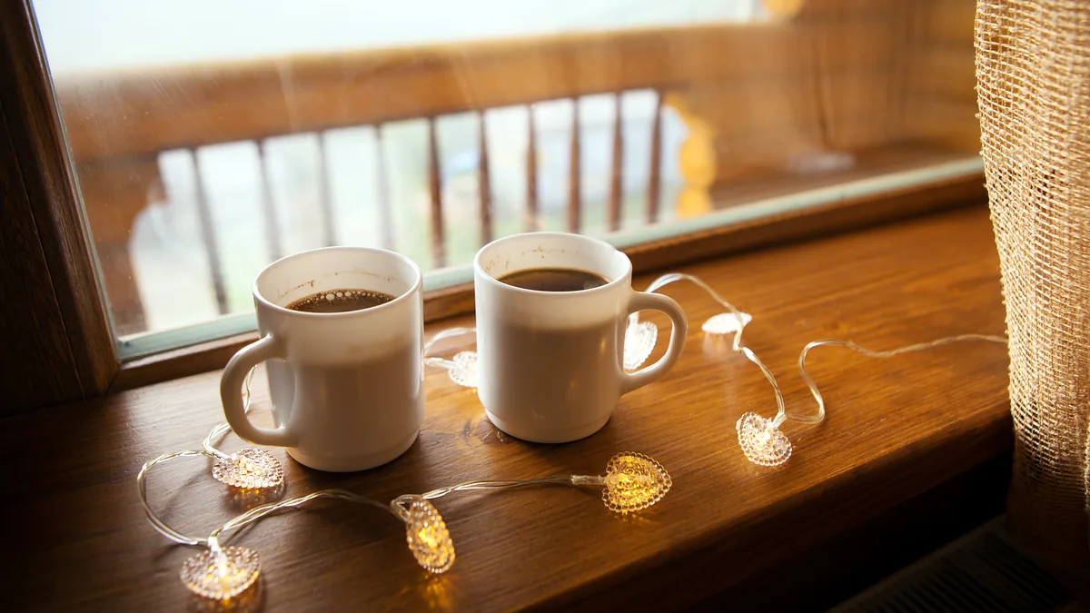 Two cups of coffee on a windowsill, steam rising in morning light.