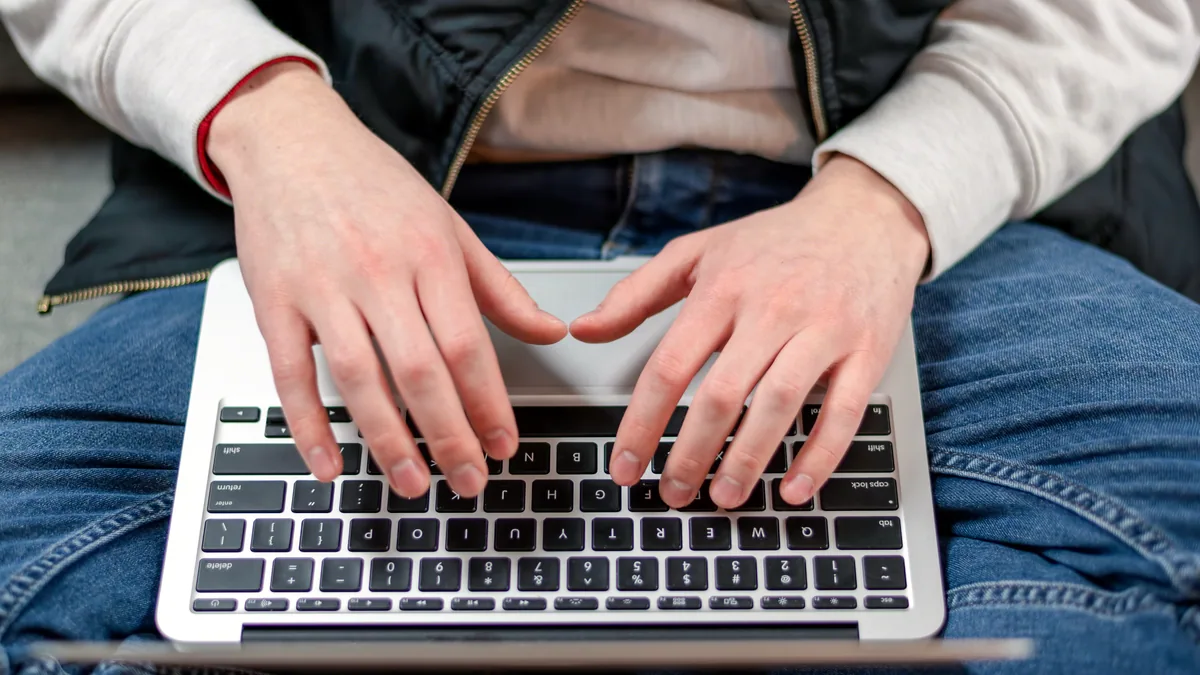Hands typing on a laptop in a bright corner of a small newsroom.