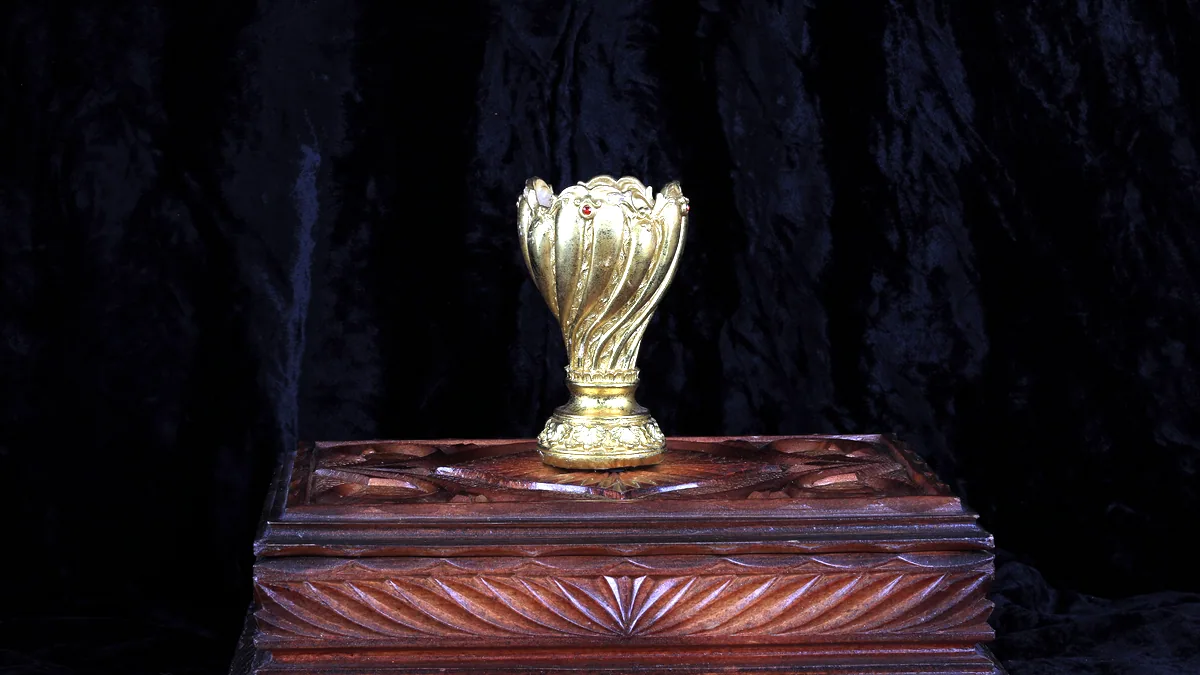 A small gold trophy standing on a wooden podium under a warm lamp.