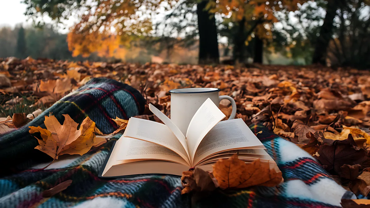 An open book lying on a bench under a tree heavy with autumn leaves.
