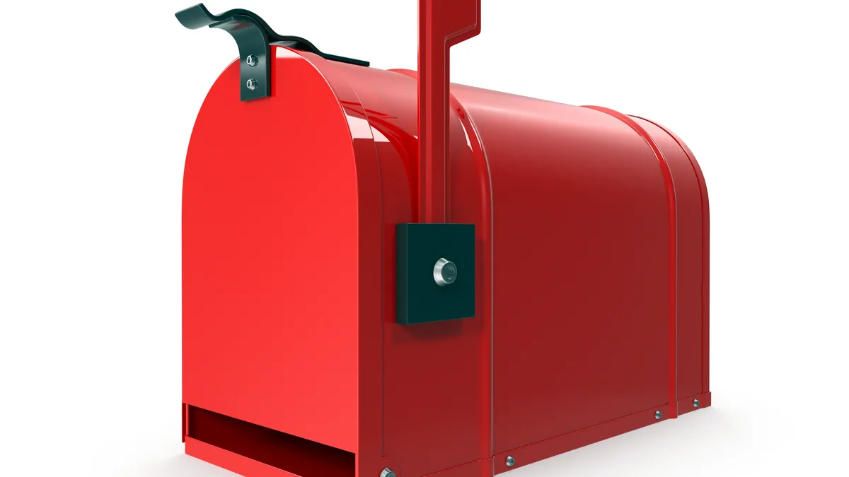 A red letterbox with its flag up on a quiet street at dawn.